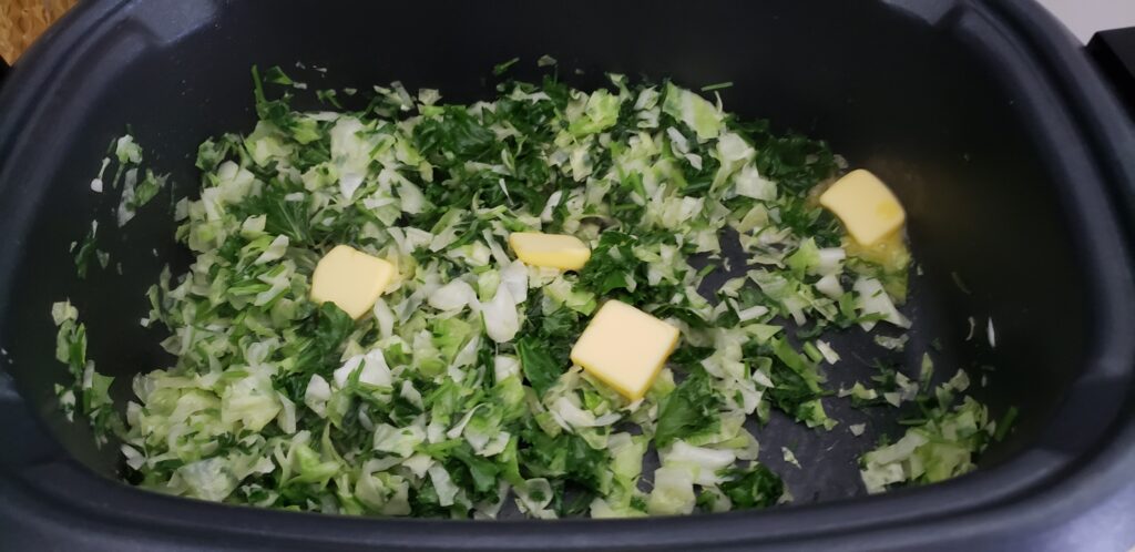 keto greens beign sauteed in a crockpot with butter in top