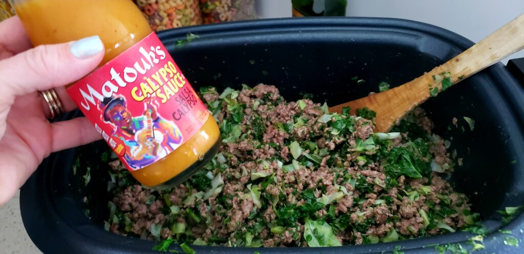 crockpot filled with keto meat and a hand holding the calypso sauce - best hot sauce