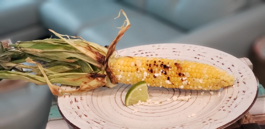 white plate with a single grilled mexican street corn on it and a lime