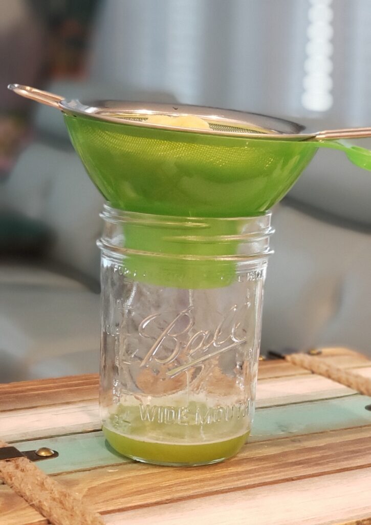 mason jar with celery juice straining from strainer on top