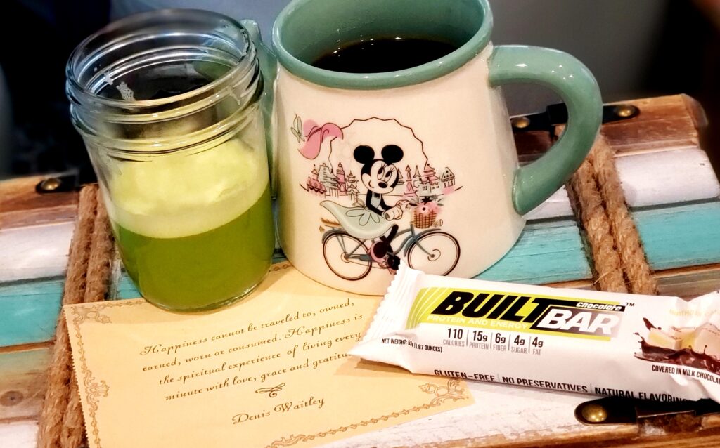 tray with a glass of green juice minnie mouse coffee cup and a protein bar with a quote