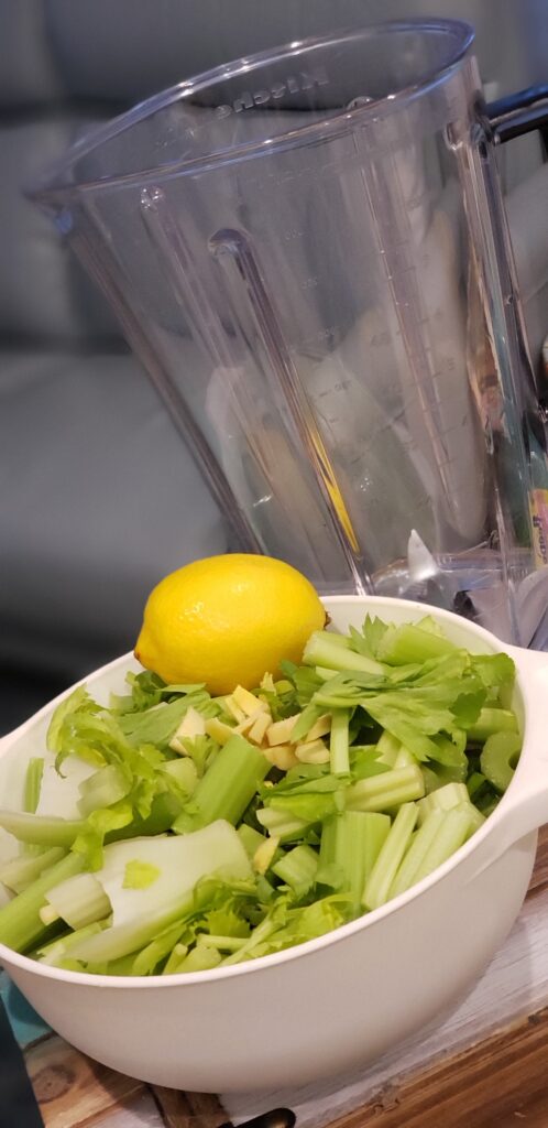 white bowl filled with celery and a lemon with empty blender next to it