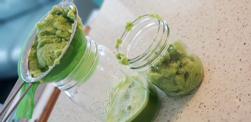 2 mason jar on counter with celery paste in a strainer and juice in the cups
