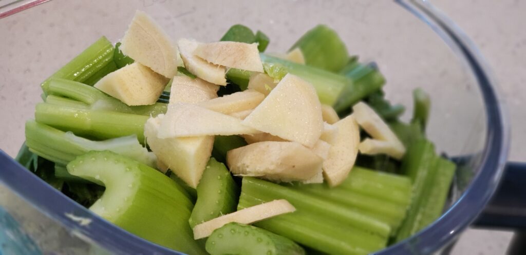 top of a blender with chopped celery and chopped fresh ginger