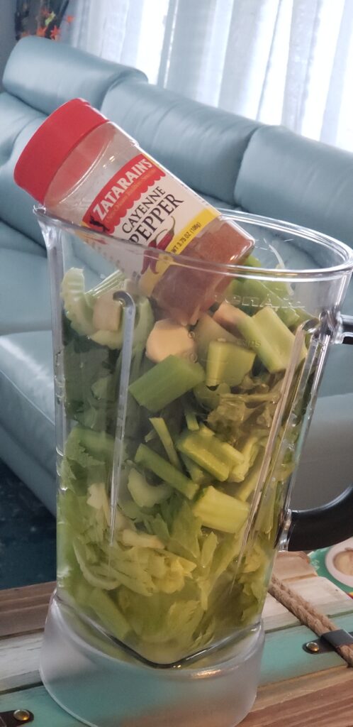 blender filled with chopped celery and a bottle of cayanne pepper sticking out of the top of it
