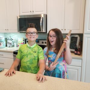 2 kids standing in a kitchen with a rolling pin
