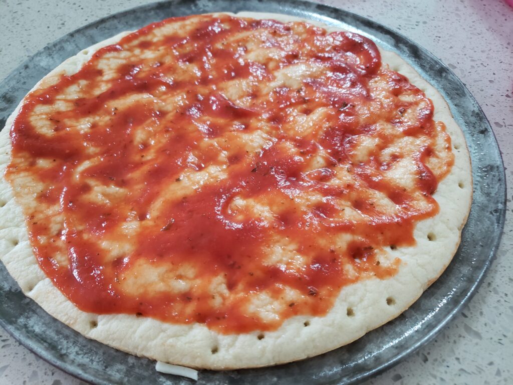 pizza crust on a pan with red sauce