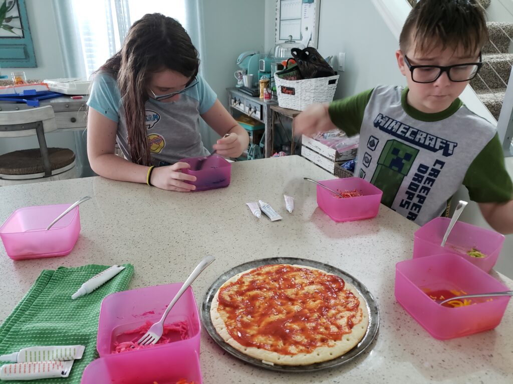 2 kids at the counter coloring cheese with food coloring in pink bowls