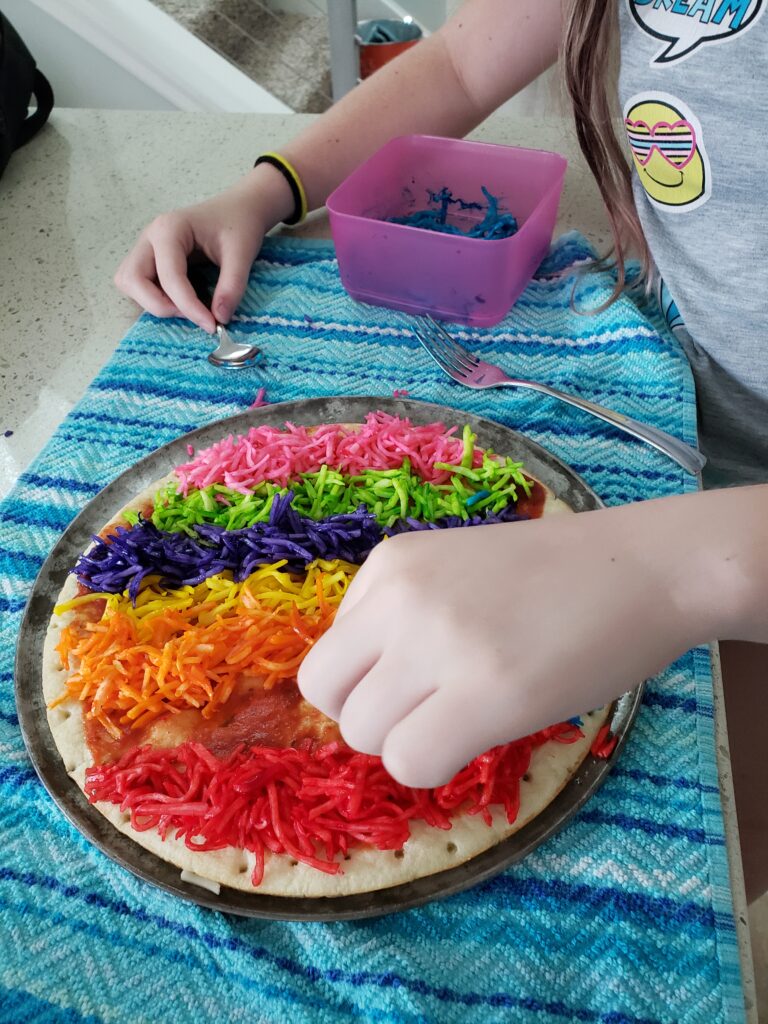 girl placing colored cheese on a crust with a pan