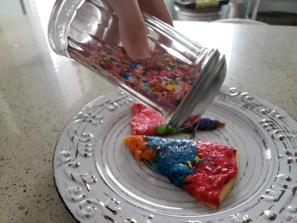 rainbow pizza - sliced with a person sprinkling sprinkles on it