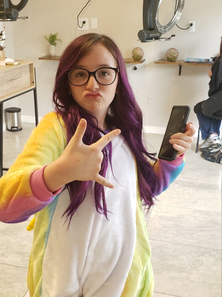 a girl in a unicorn onesies making a face with purple hair