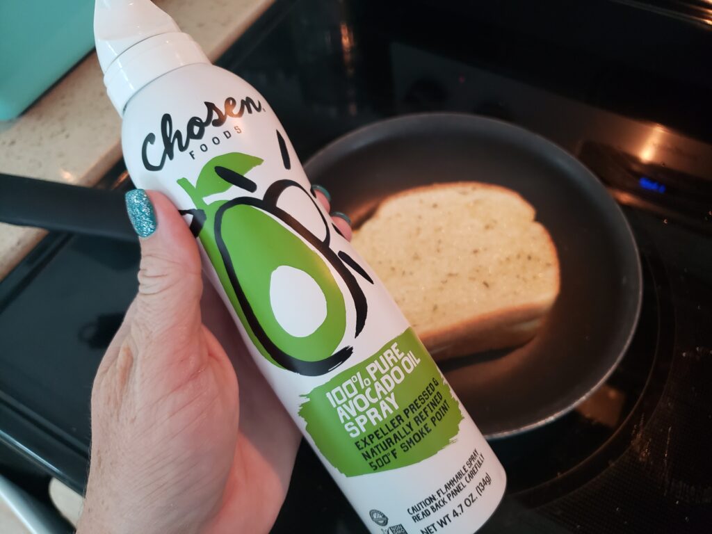 grilled cheese in a pan with avocado spray in a woman's hand over the pan
