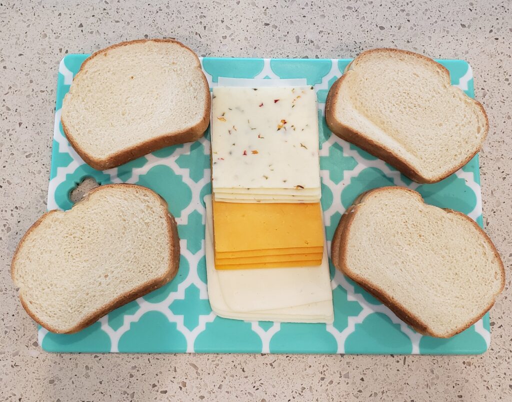 4 slices of bread on a cutting board with cheese in the middle