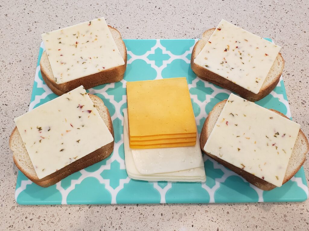 bread on a cutting board with 1st slice of cheese on the bread