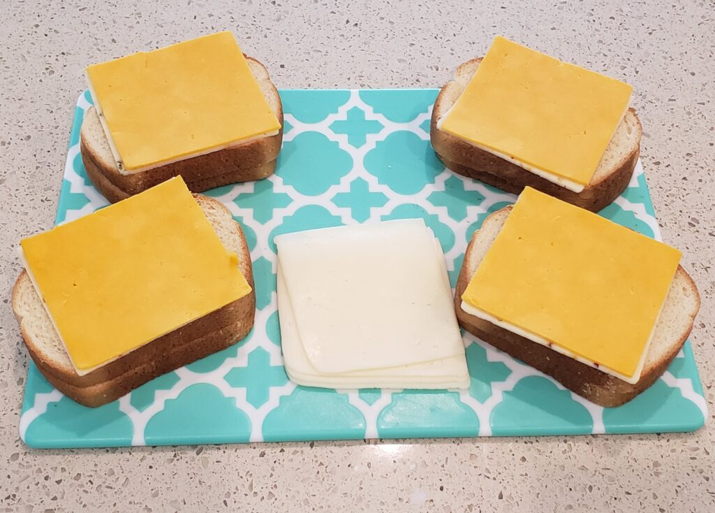 bread on a cutting board with 2nd slice of cheese on the bread