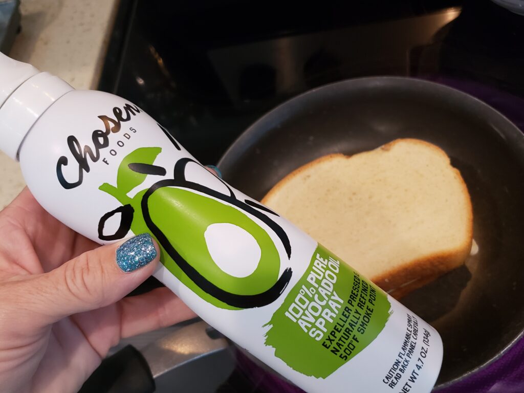 avocado spray in a womans hand over a pan of grilled cheese
