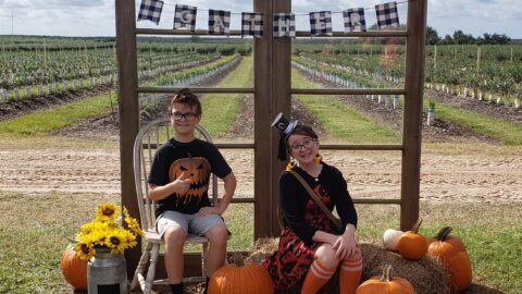 2 kids sitting with pumpkins and hay for a picture