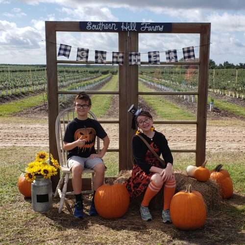 2 kids sitting with pumpkins and hay for a picture