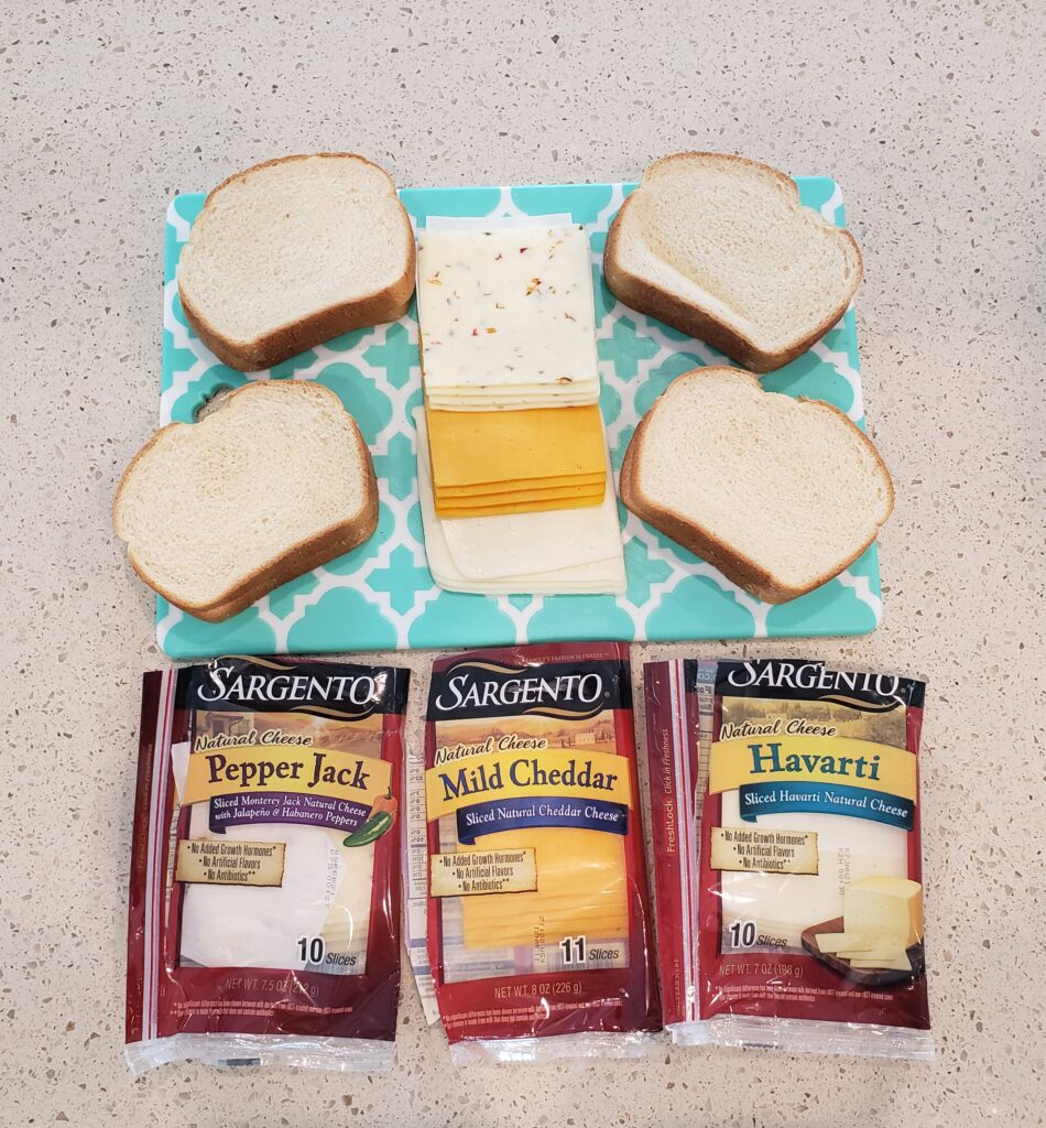 4 slices of bread on a cutting board with cheese in the middle and the packages of cheese in front