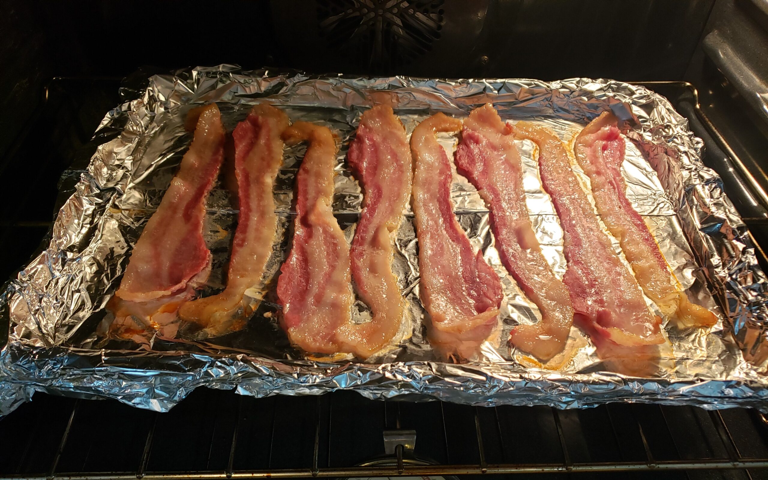 bacon on tinfoil on a pan in the oven