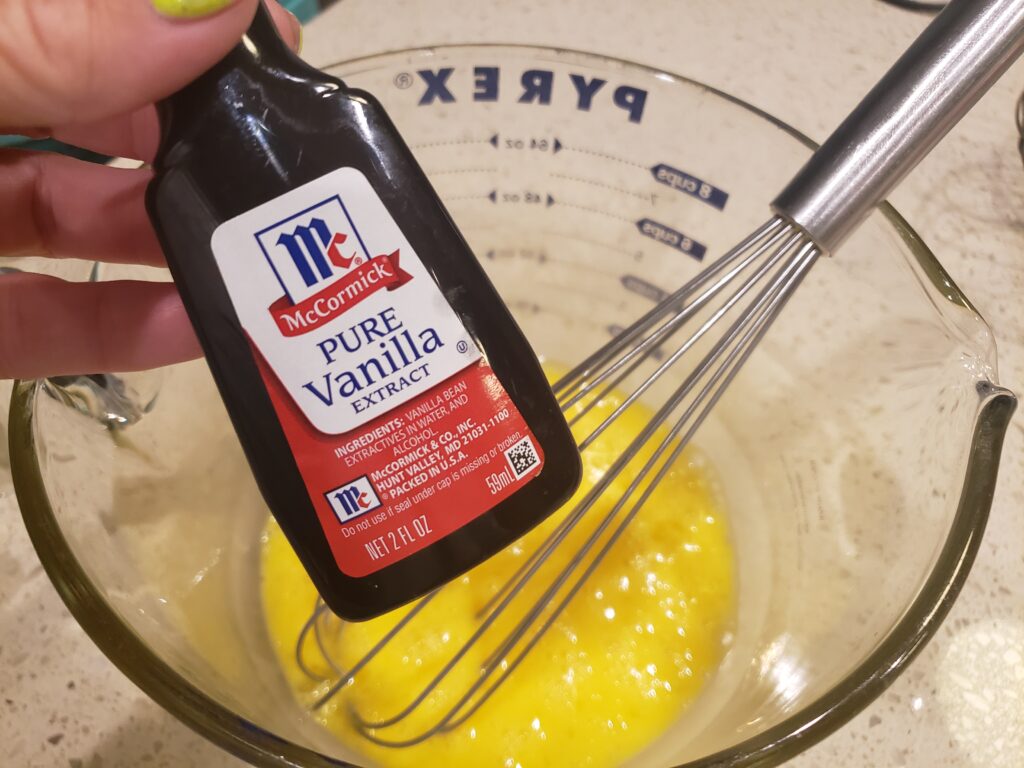 eggs cracked and beaten in a bowl with vanilla extract above it