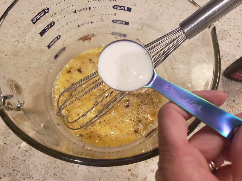 egg batter in a bowl with a wire beater in it and cream above it
